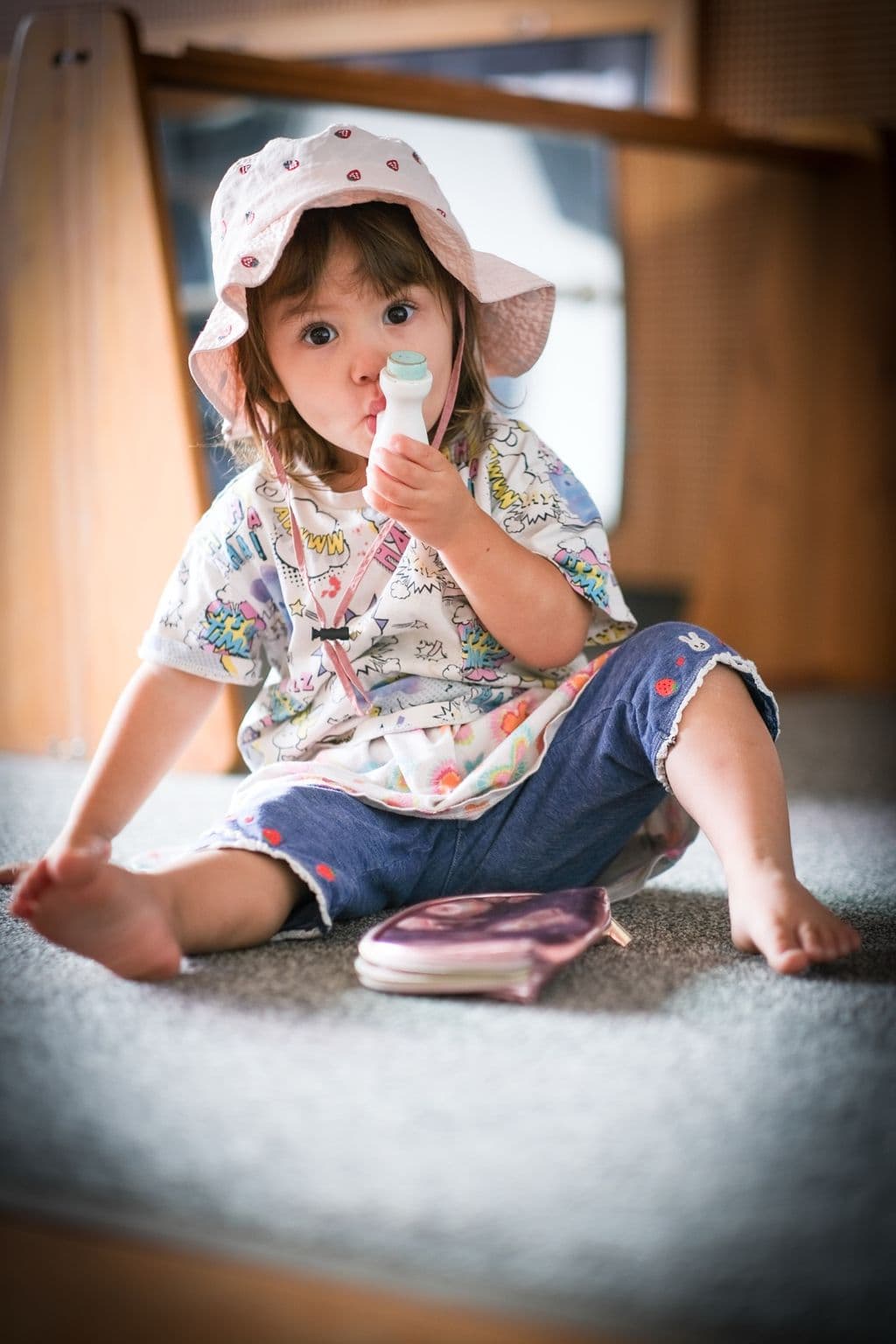 Toddler in a sun hat exploring a small bottle during practical life play at Triton Montessori Educare