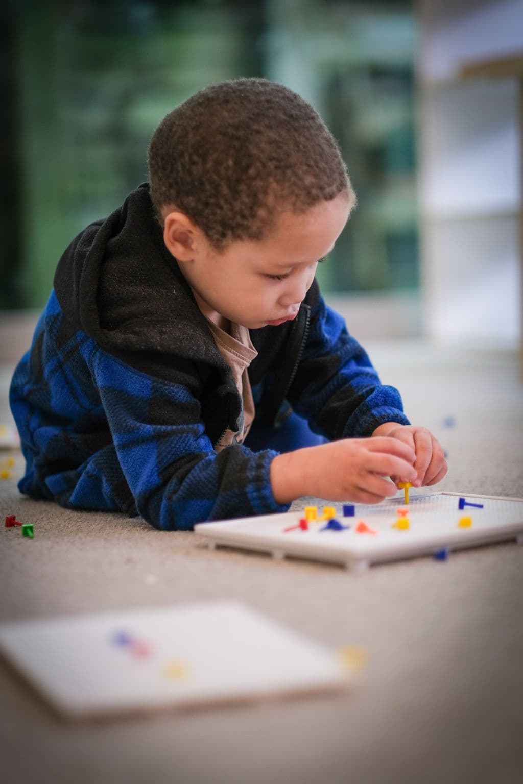 Preschool child carefully placing coloured pegs in a pattern activity, developing fine motor skills and focus