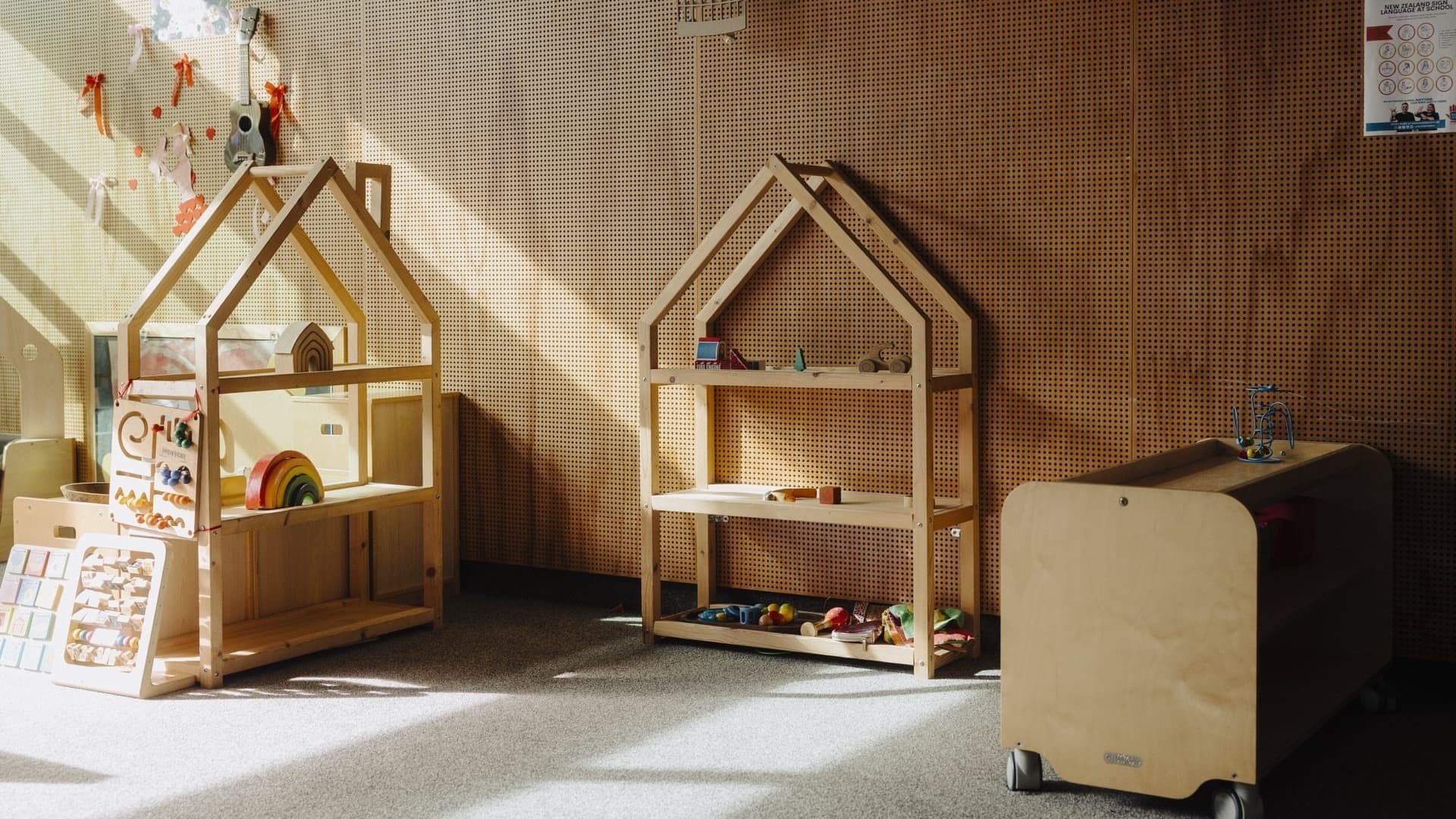 Wooden house-shaped classroom shelves with Montessori materials in warm sunlight