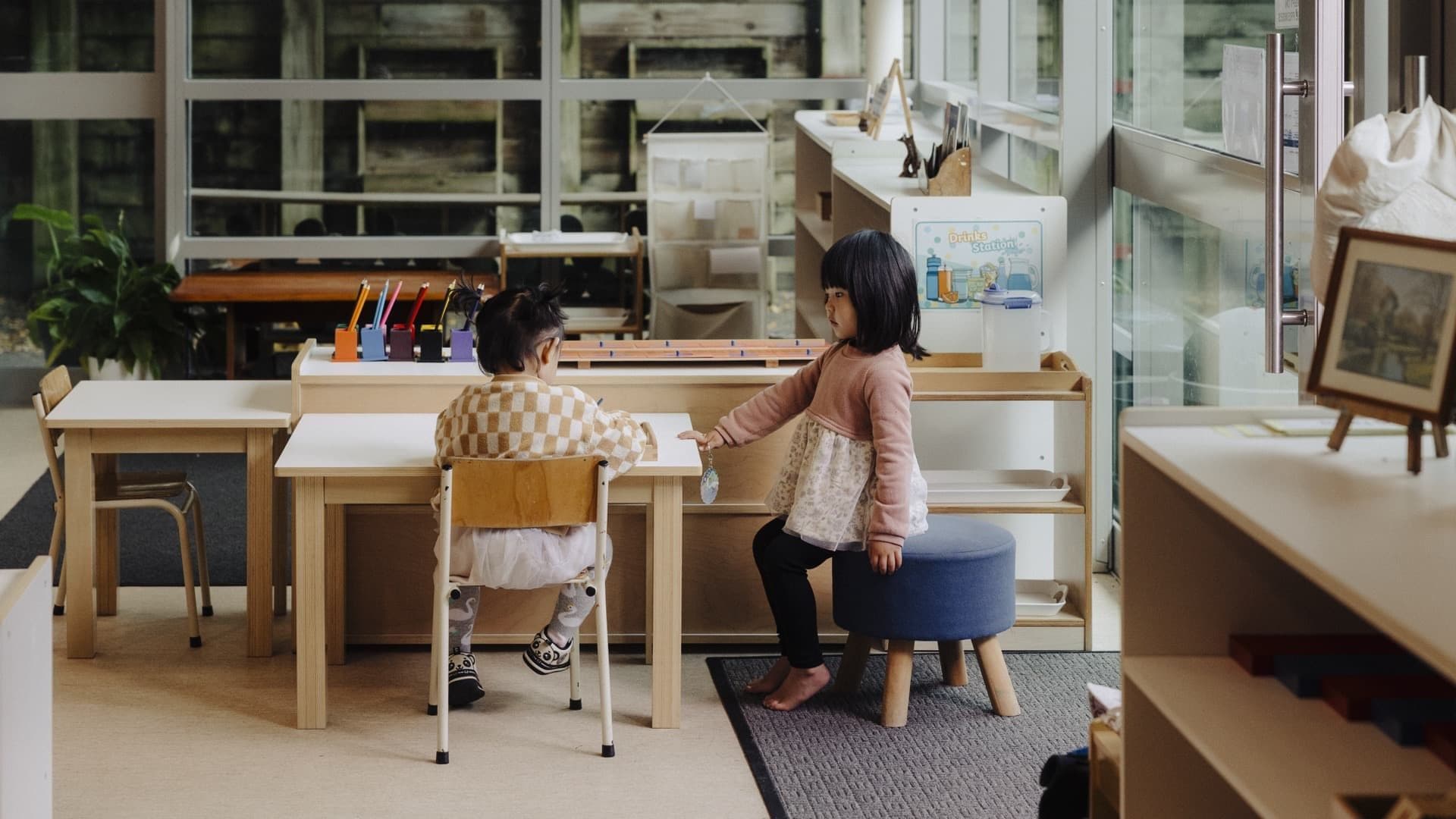 Two children sitting at a classroom table with a kaiako nearby at Triton Montessori Educare