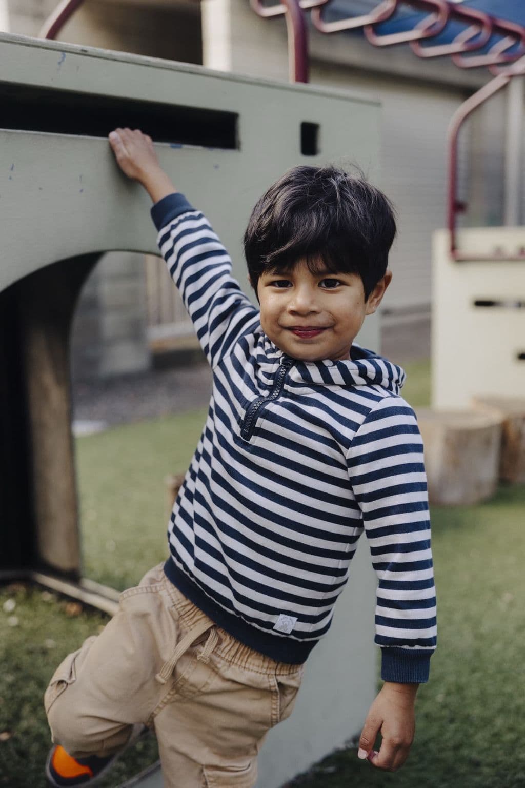 Preschool child in a striped hoodie playing near outdoor climbing equipment at Triton Montessori Educare