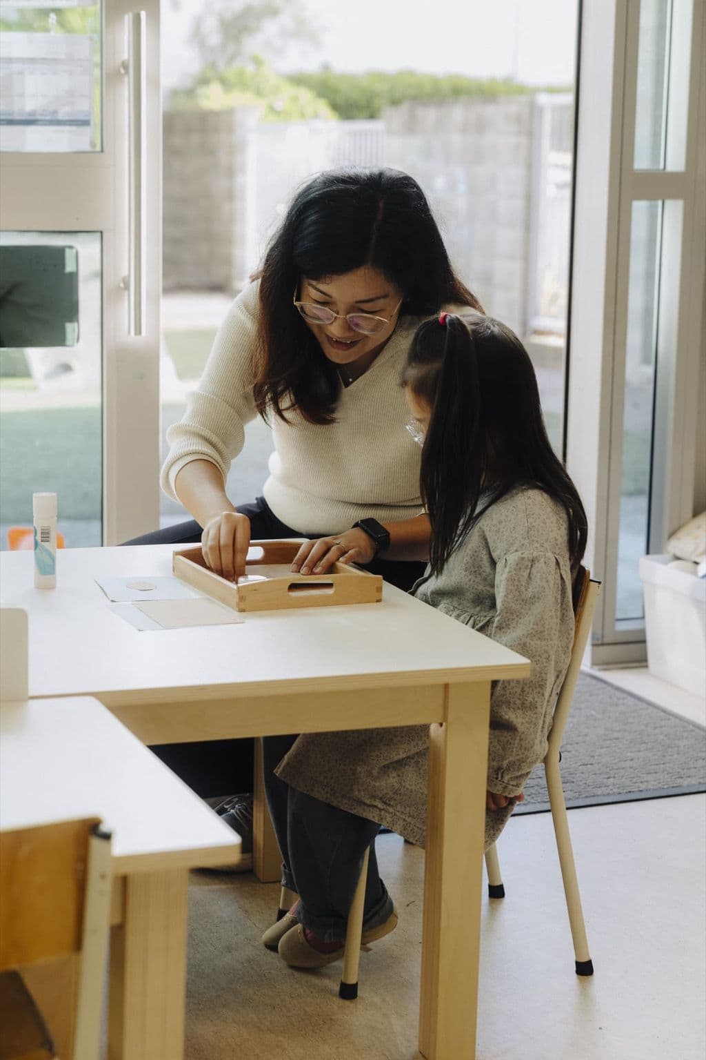 Kaiako supporting a child with a Montessori learning activity at a classroom table