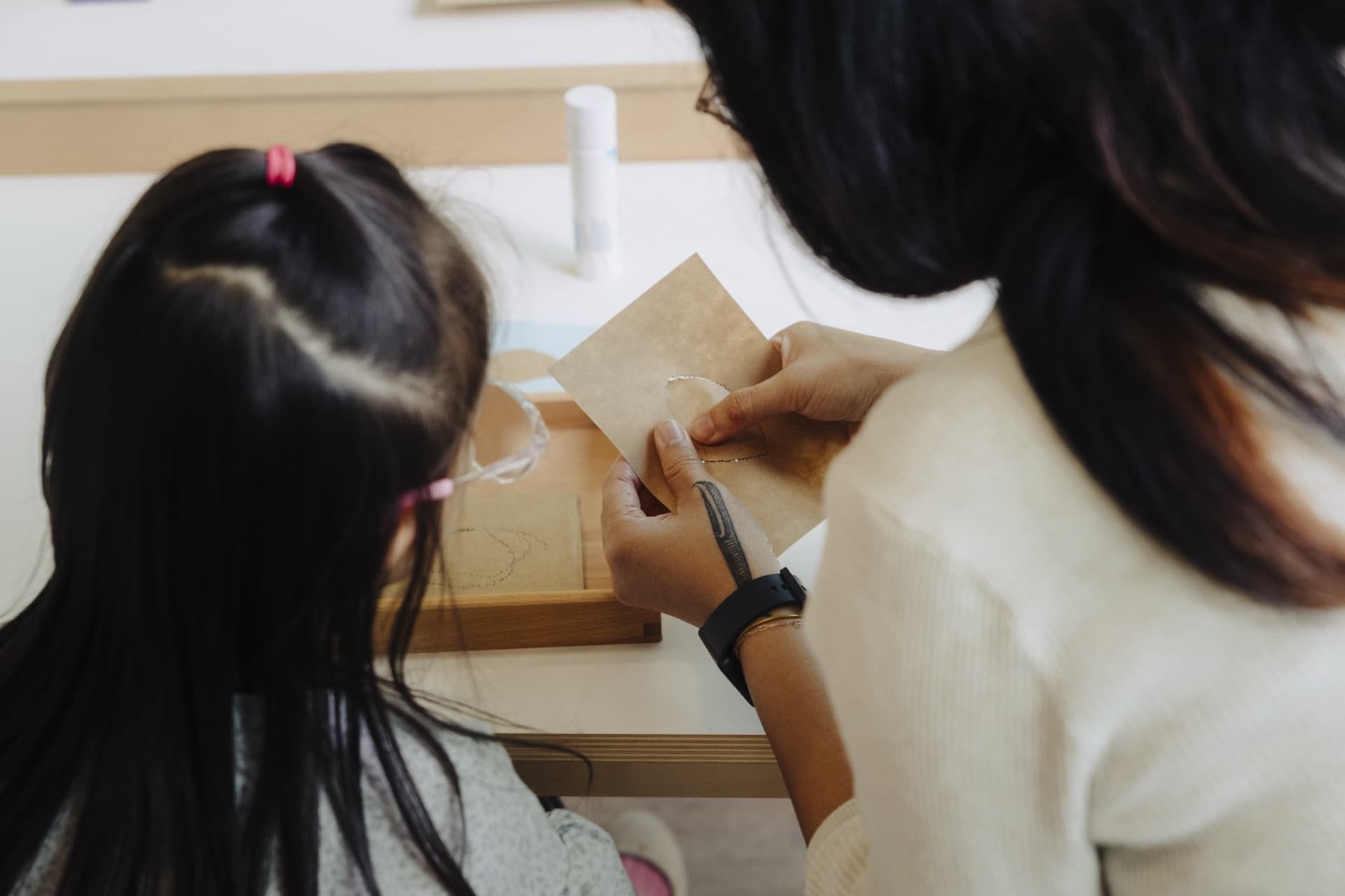Close-up of a child and kaiako working with a wooden Montessori material
