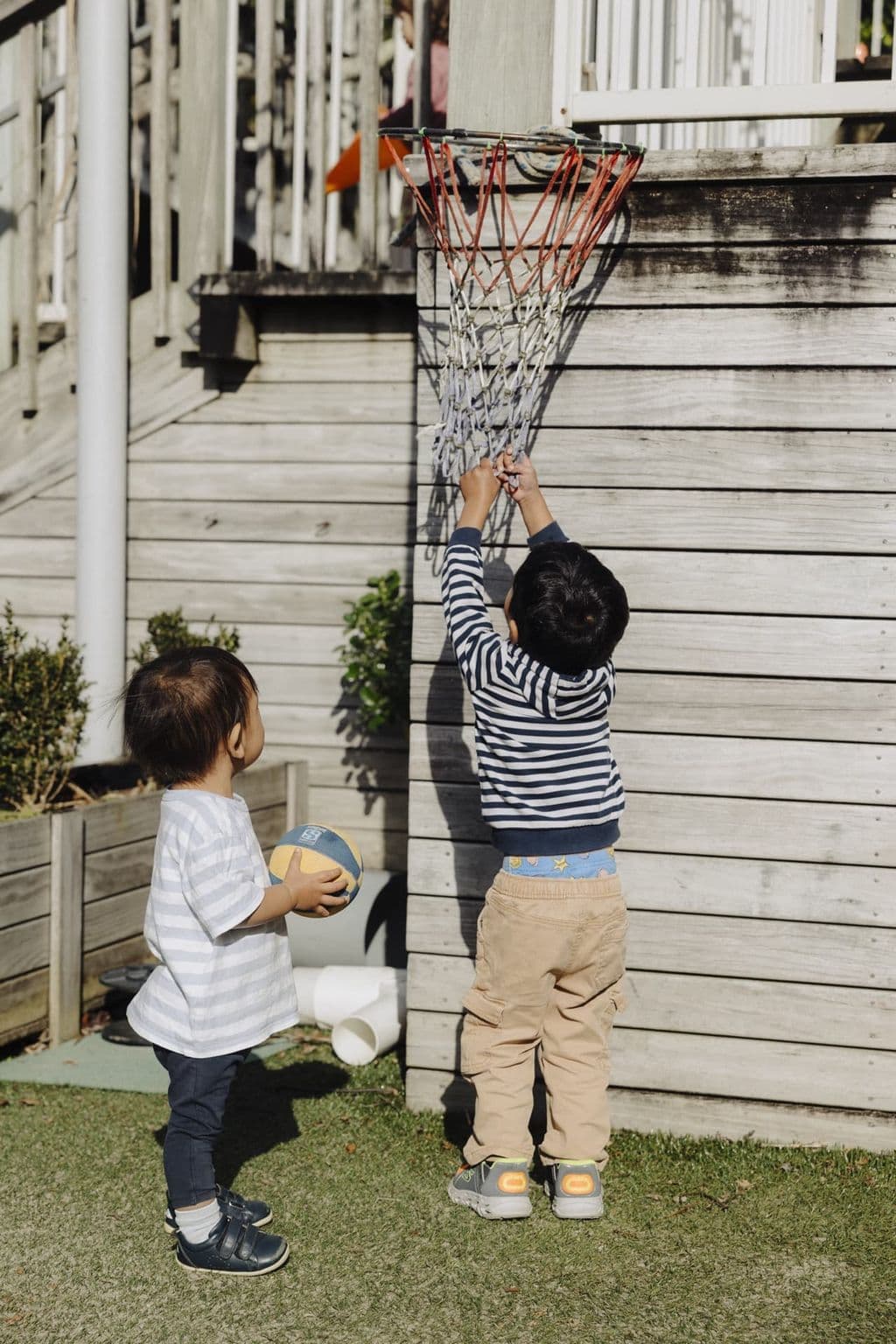 Children playing with a basketball hoop in the outdoor garden at Triton Montessori Educare